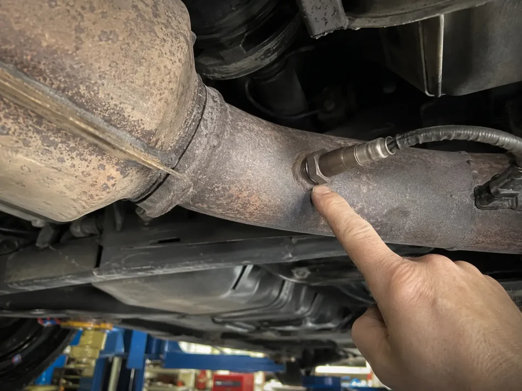 Close up of a downstream oxygen sensor threaded into a dirty exhaust pipe — proves what the component looks like under real vehicle conditions