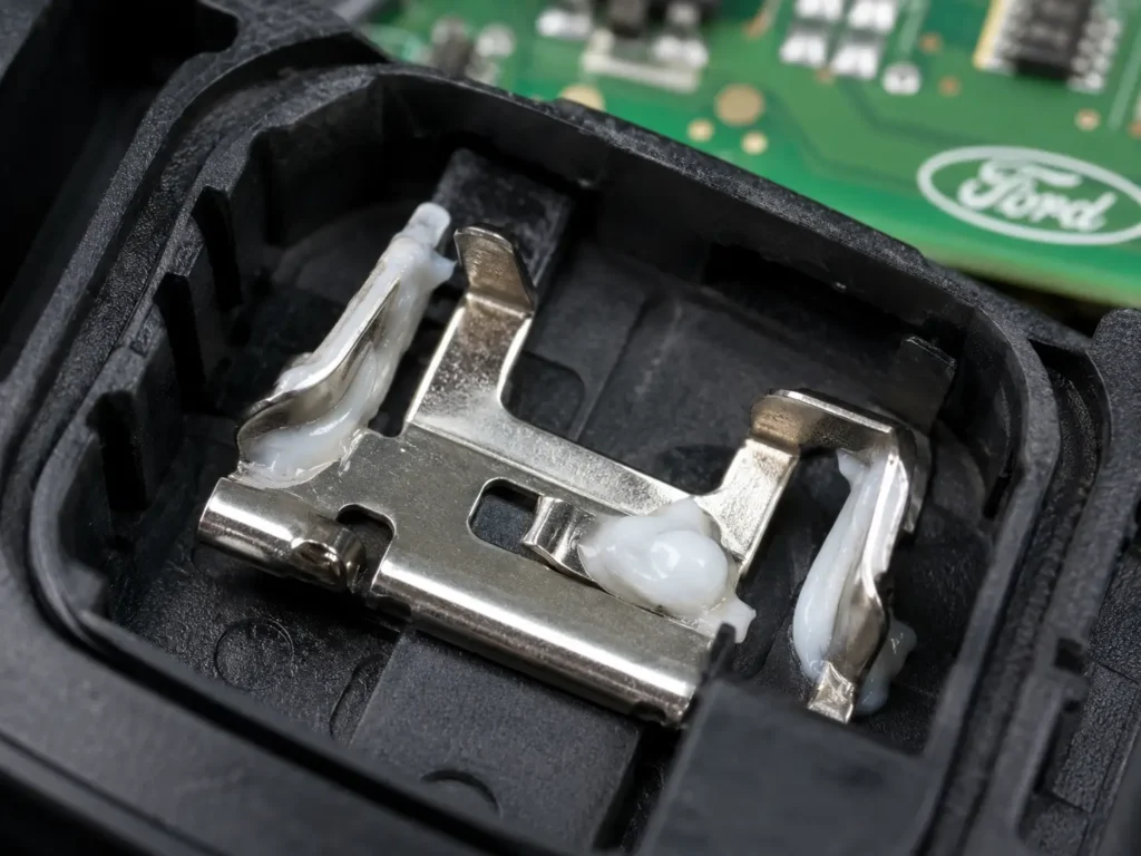 How to Change Battery in Ford Key Fob — Complete Guide 2026 (All Models) 8 Extreme macro close-up of a Ford key fob battery terminal with white dielectric grease applied to the metal contacts and the circuit board visible in the background.