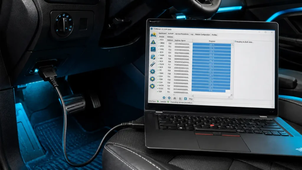 How to Calibrate Ford SYNC: APIM Diagnostics and System Reset Guide 2026 5 Laptop running FORScan software on a car seat, connected by cable to the OBD2 port under the dashboard, with blue cabin lighting and diagnostic data visible on screen.