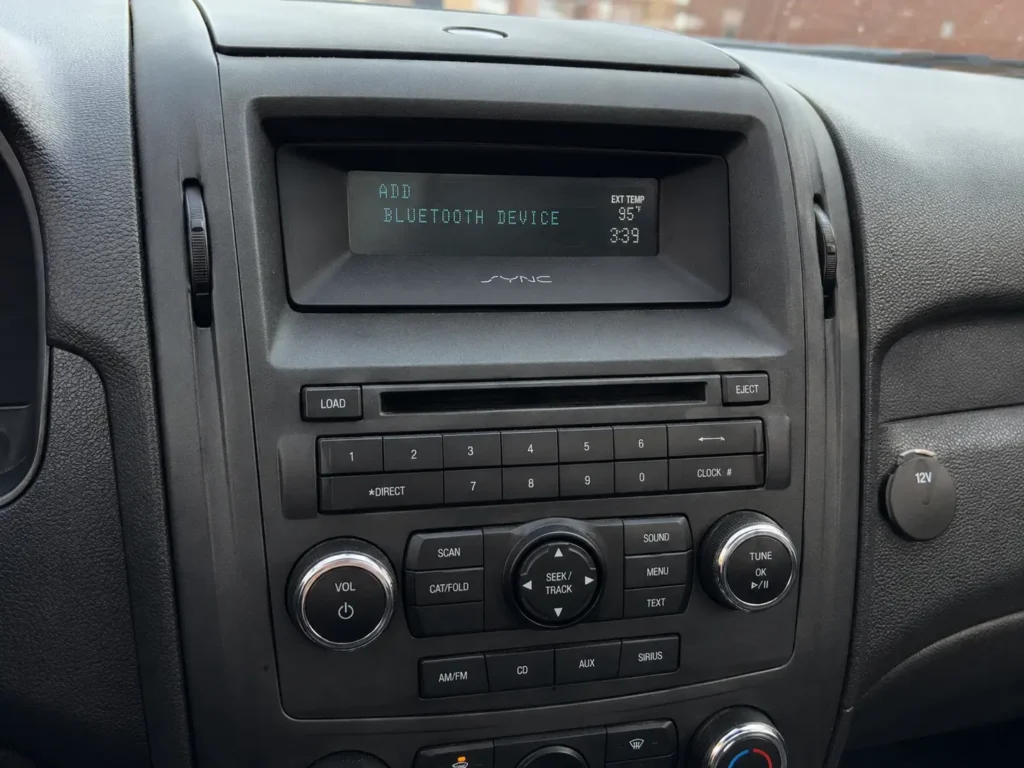 How to Connect Phone to Ford SYNC to Play Music (All Versions) 3 Ford SYNC 1 monochrome dashboard display showing “ADD BLUETOOTH DEVICE” with physical audio control buttons below.