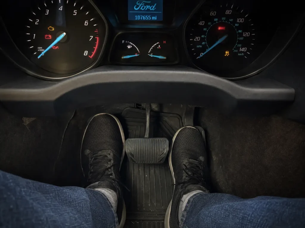 2016 Ford Escape Oil Reset — 3 Methods + Engine Oil Specs for All Engines 4 Inside a 2016 Ford Escape showing a driver pressing the brake and accelerator pedals while the dashboard is lit in accessory mode.