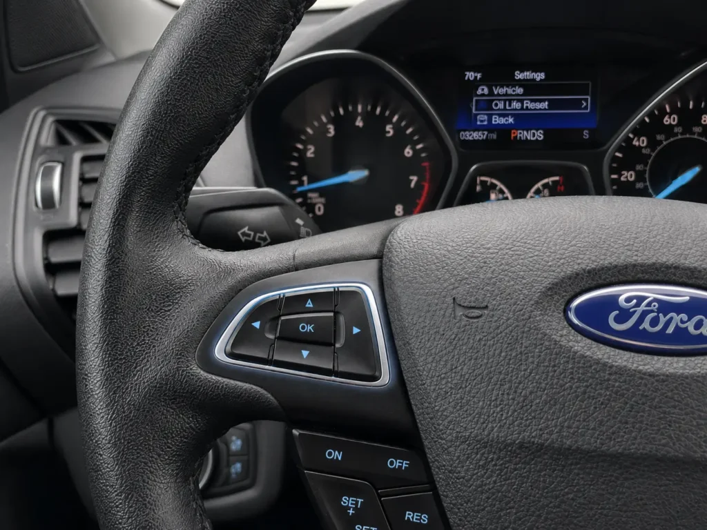 Close-up of 2017 Ford Escape steering wheel left-side directional pad with instrument cluster Settings menu in the background.