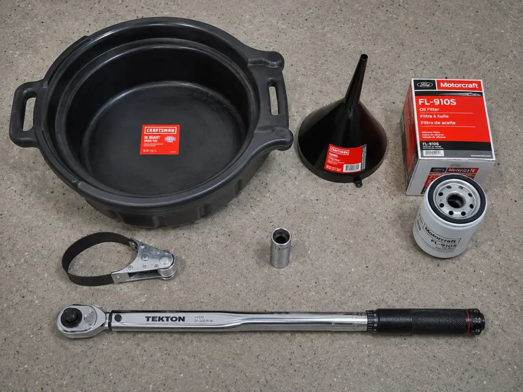 Overhead flat lay of oil change tools including a 13mm socket, torque wrench, oil filter wrench, drain pan, funnel, and Motorcraft FL-910S oil filter box.