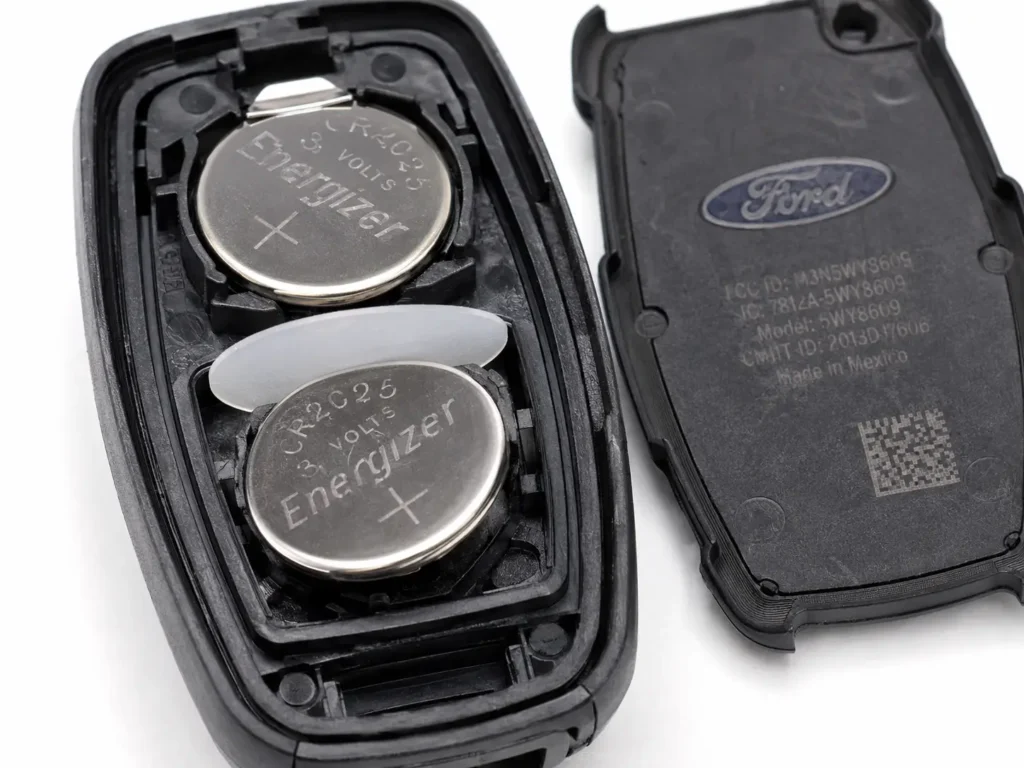 Macro close-up inside an opened 2014 Ford Fusion smart key fob showing two stacked CR2025 batteries separated by a thin round plastic disc.