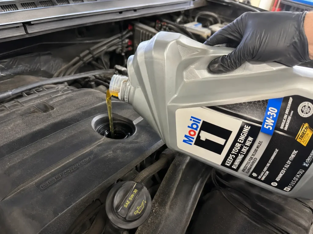 Ford 3.5 EcoBoost Oil Capacity Chart 2011 to 2025 All Variants 3 Mechanic pouring 5W-30 oil into Ford F-150 3.5 EcoBoost engine filler cap during oil change